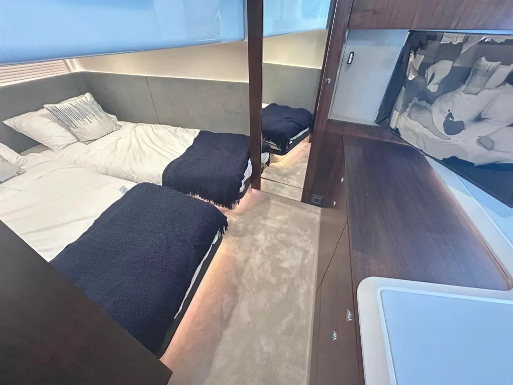 A stylish boat cabin with two single beds, navy blankets, wooden furniture, and soft lighting for a cosy atmosphere.